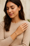 Woman wearing a delicate gold bracelet with red gemstone accents on her wrist