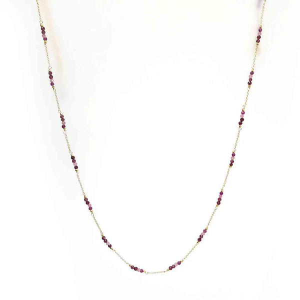 Gold chain necklace with evenly spaced small red beads on white background