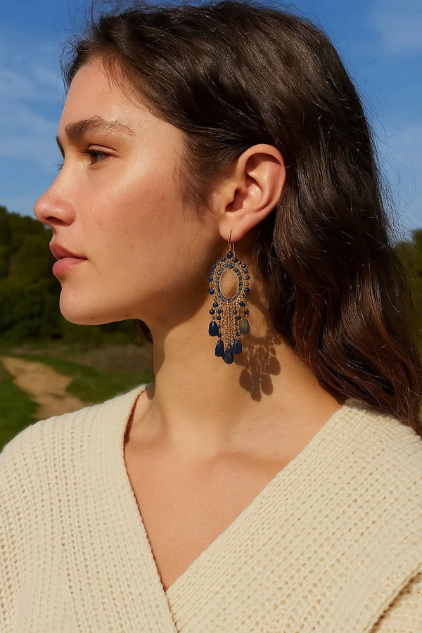 Woman wearing boho-style gold and blue statement dangle earrings outdoors